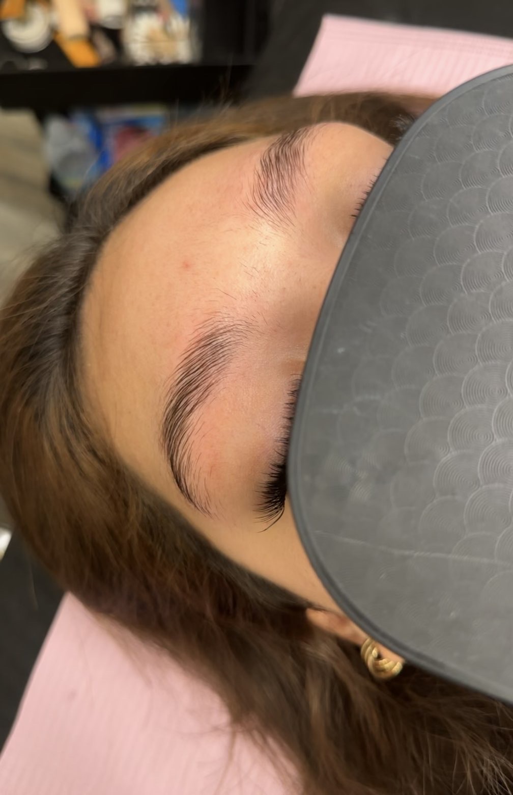 Before: the client's natural brows brushed upward, uneven in shape, as she lies on the treatment bed.